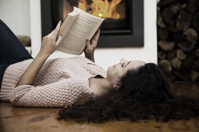 Lady lying on the floor and reading a book on branding, by the fireplace.