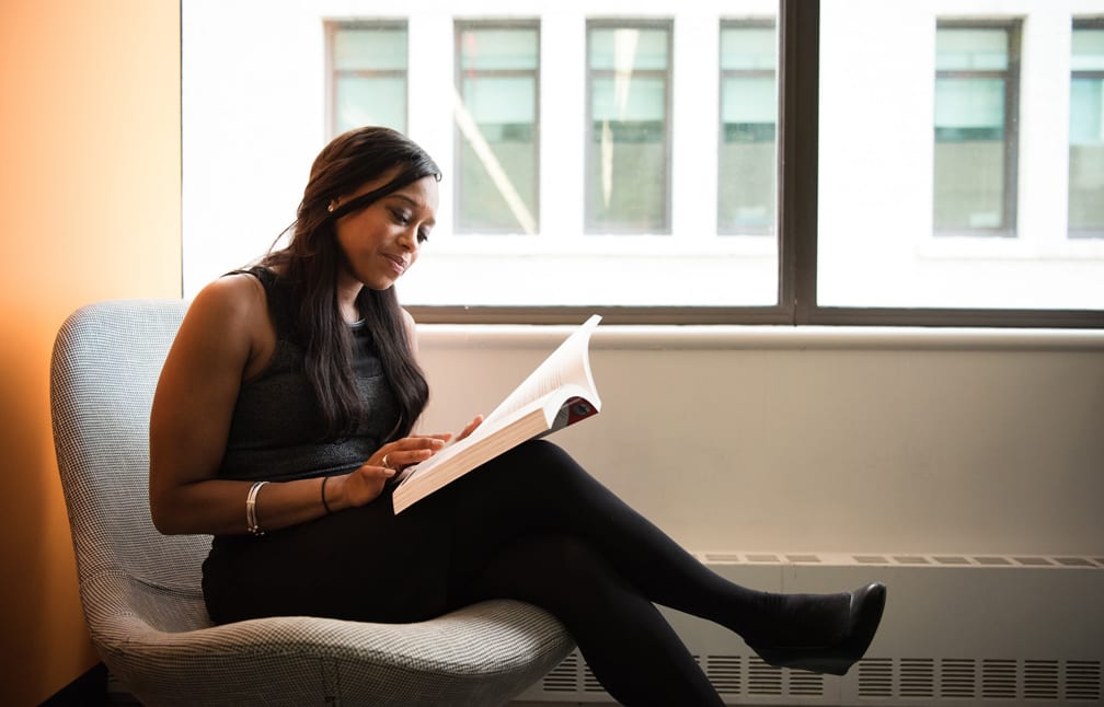 Young African woman reading a book near an office window at a copywriting course in Singapore.